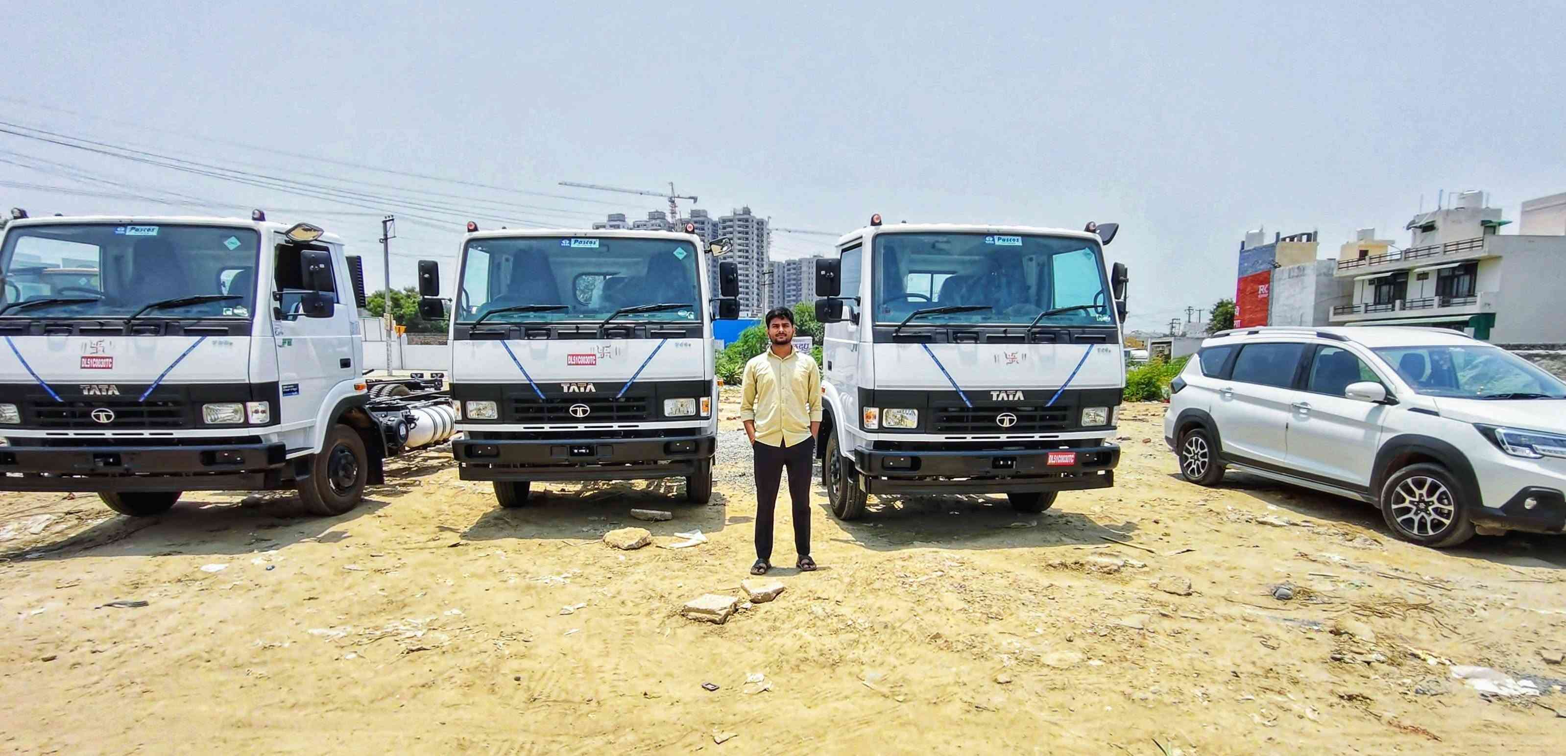 A man standing between three white Tata trucks parked on an open lot
