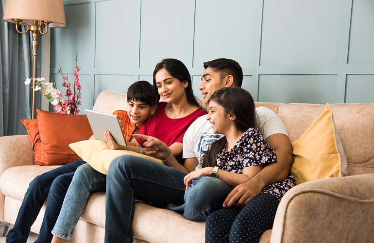 Indian family using smartphone, laptop or tablet, watching movie, surfing internet, sitting on sofa